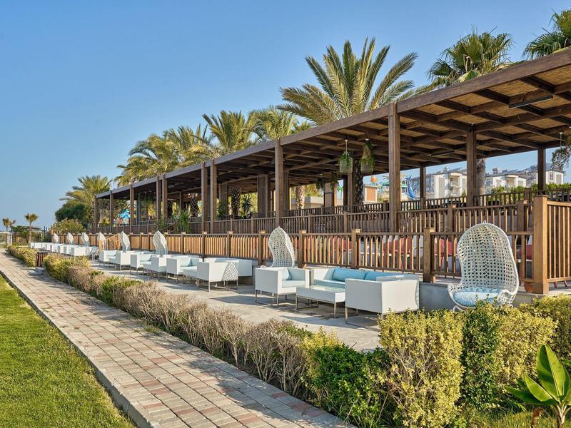 Salon extérieur moderne avec sièges blancs et toit en bois, palmiers en arrière-plan.