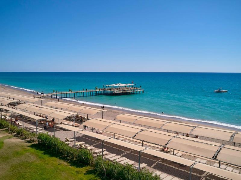 Vue côtière avec une longue jetée, plage de sable et ciel bleu clair.
