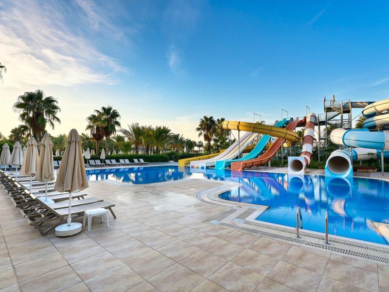 Espace piscine avec toboggans aquatiques, chaises longues et parasols par une journée ensoleillée.