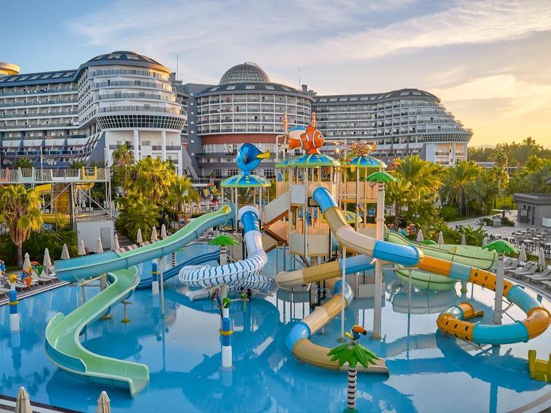 Parc aquatique avec des toboggans colorés et un hôtel en arrière-plan au coucher du soleil.