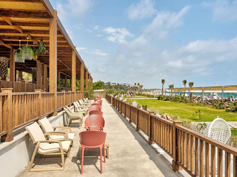 Une terrasse avec des sièges donnant sur un jardin et la mer par une journée ensoleillée.