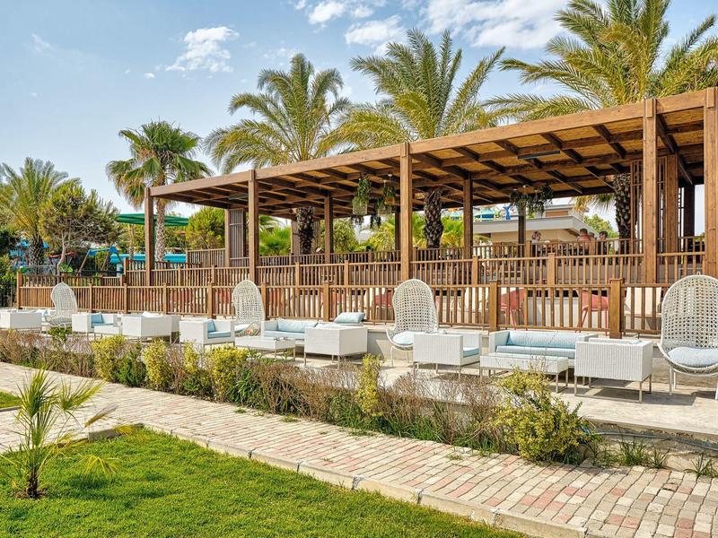 Espace piscine avec chaises longues blanches et pergola en bois entourée de palmiers et de verdure.