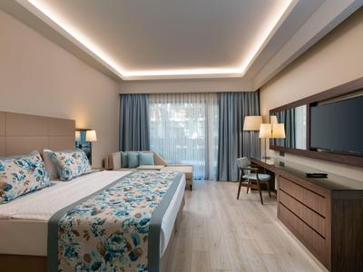 Modernes Hotelzimmer mit großem Bett, hellen Holzmöbeln und einem Fenster mit blauen Vorhängen.