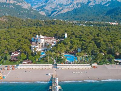 Hotelanlage am Strand mit Pool, grüner Umgebung und Bergen im Hintergrund.