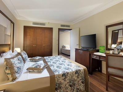 Gemütliches Schlafzimmer mit großem Bett, Holzmöbeln, TV und Schreibtisch in warmen Farben.