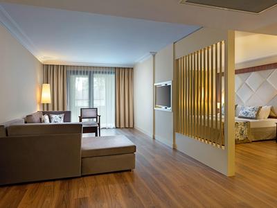 Modernes Wohnzimmer mit Sofaecke, Holzboden, großem Fenster und Zugang zu einem Schlafzimmer.