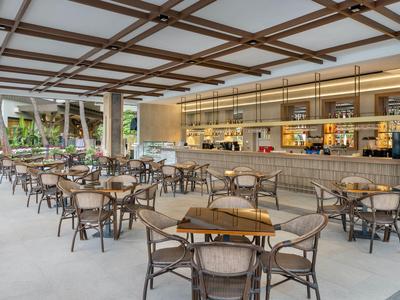 Offener Hotelrestaurantbereich mit Holztischen, Stühlen und einer Bar im Hintergrund.