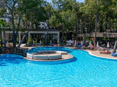 Großer Hotelpool mit blauem Wasser, umgeben von Liegestühlen und Bäumen.