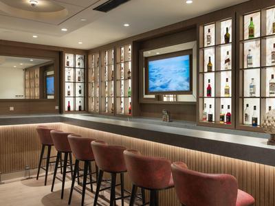 Moderne Hotelbar mit Theke, gepolsterten Barhockern und beleuchteten Regalen mit Flaschen.