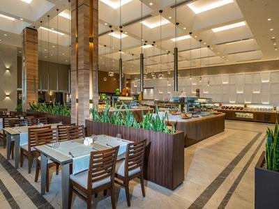 Moderner Hotelrestaurant-Innenraum mit Holzmöbeln, Buffetbereich und dekorativen Pflanzen.