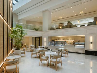 Helles, modernes Hotelrestaurant mit weißen Tischen, Holzstühlen und großen Fenstern.