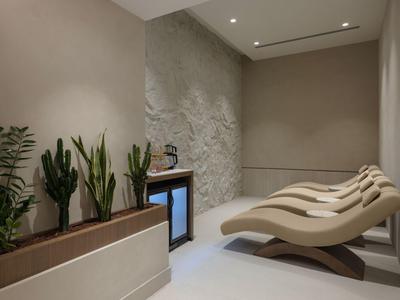 Moderner Spa-Ruheraum mit geschwungenen Liegen und grünen Pflanzen vor einer weißen Steinwand.