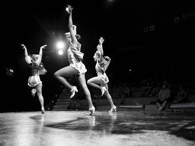 Tre ballerine eseguono una coreografia sul palco davanti a un pubblico.