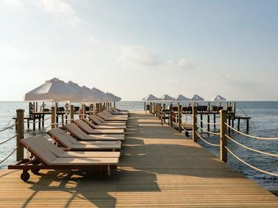 Langer Holzsteg mit Liegestühlen und Sonnenschirmen neben ruhigem Meer unter klarem Himmel.