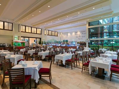 Großer, heller Speisesaal mit vielen Tischen, weißen Tischdecken und roten Stuhlkissen.