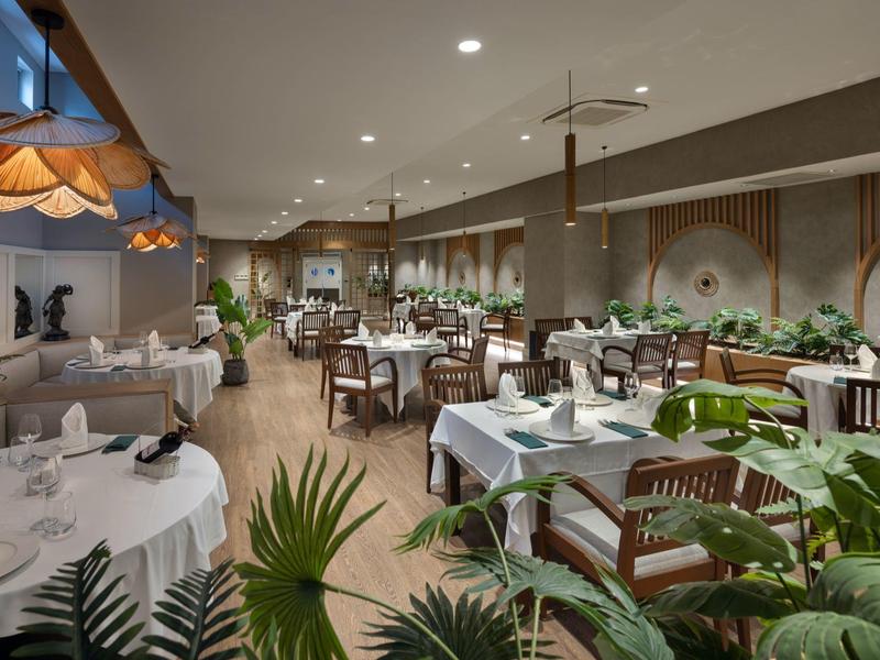 Elegantes Restaurant mit gedeckten Tischen, grünen Pflanzen und sanfter Beleuchtung.