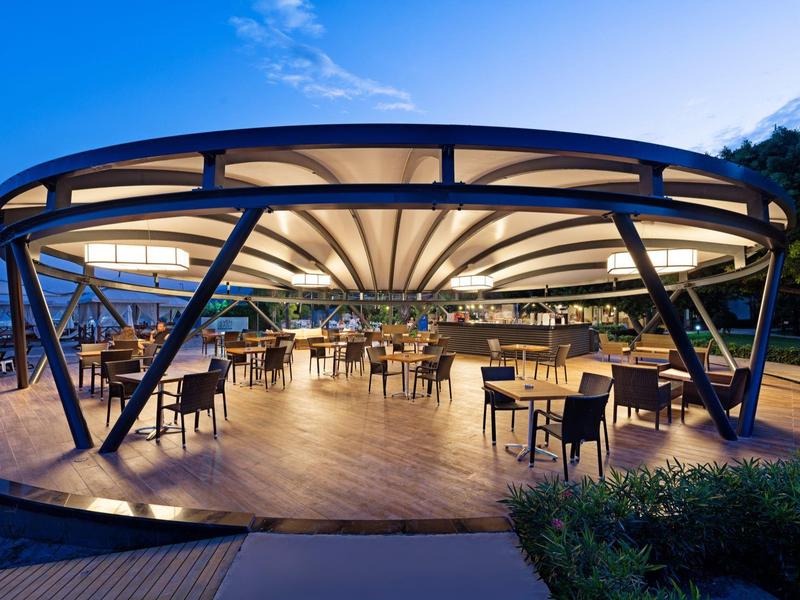Modernes, offenes Restaurant mit beleuchtetem Zeltdach und Tischen im Außenbereich bei Dämmerung