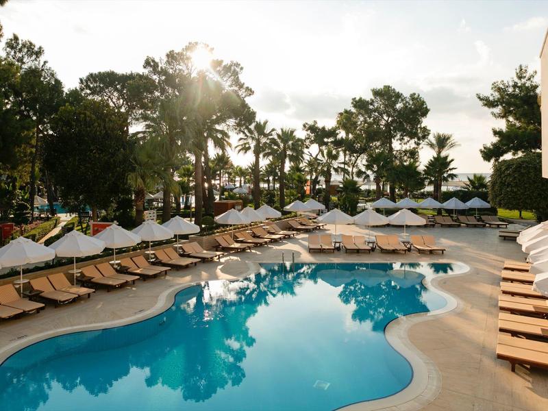 Ein Schwimmbad mit blauer Wasseroberfläche, umgeben von Liegestühlen und weißen Sonnenschirmen.