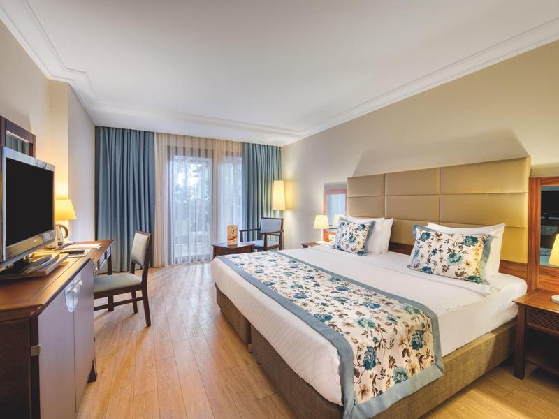 Gemütliches Hotelzimmer mit großem Bett, Holzfußboden und Balkon hinter blauen Vorhängen.