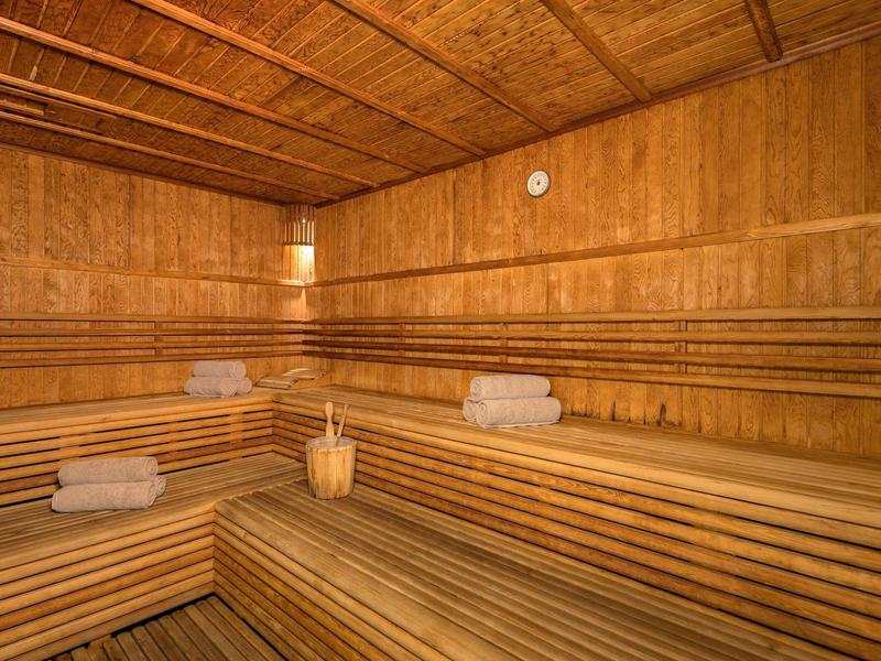 Holzsauna mit mehrstufigen Sitzbänken, handtüchern und einem Holzeimer mit Kelle.