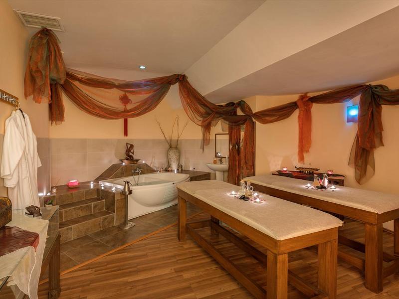 Gemütlicher Wellnessraum mit Holzliegen, Badewanne und braunen Stoffvorhängen an der Decke.