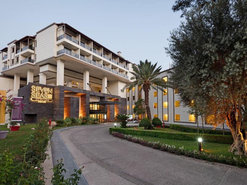 Großes Hotelgebäude mit Palmen, gepflegtem Garten und beleuchtetem Eingangsbereich am Abend.