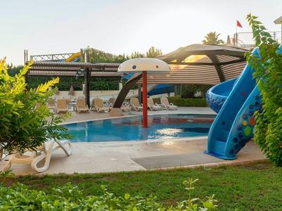 Basen dla dzieci z fontanną i zjeżdżalnią obok leżaków w ogrodzie hotelowym