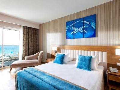 Helles Schlafzimmer mit großem Bett, blauem Bettüberwurf, Meerblick und moderner Wandkunst.