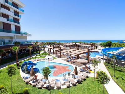 Widok na basen hotelowy z parasolami, leżakami i zjeżdżalniami wodnymi nad morzem.