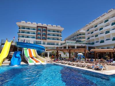 Basen z kolorowymi zjeżdżalniami przed nowoczesnym hotelem z tarasami i leżakami.