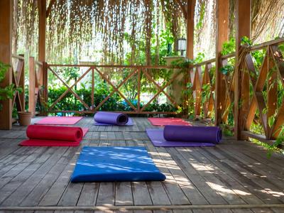 Dřevěná zastřešená plošina s barevnými jógovými podložkami v tropickém prostředí.