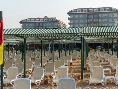 Lege strandstoelen onder groene zonneschermen voor twee grote hotelgebouwen.