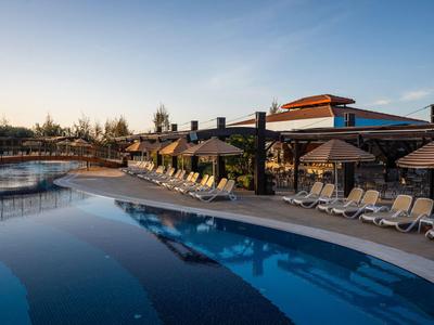 Modern hotelzwembad met ligstoelen en parasols bij zonsondergang.