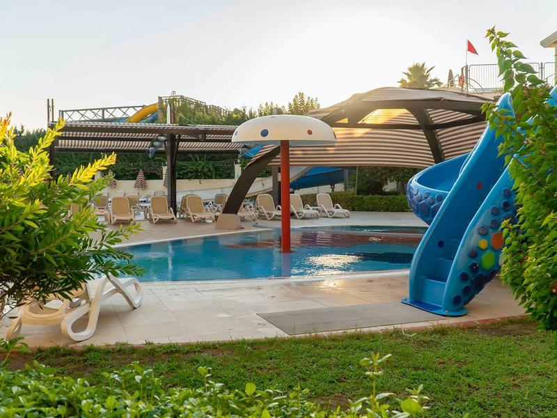 Basen dla dzieci z fontanną i zjeżdżalnią obok leżaków w ogrodzie hotelowym