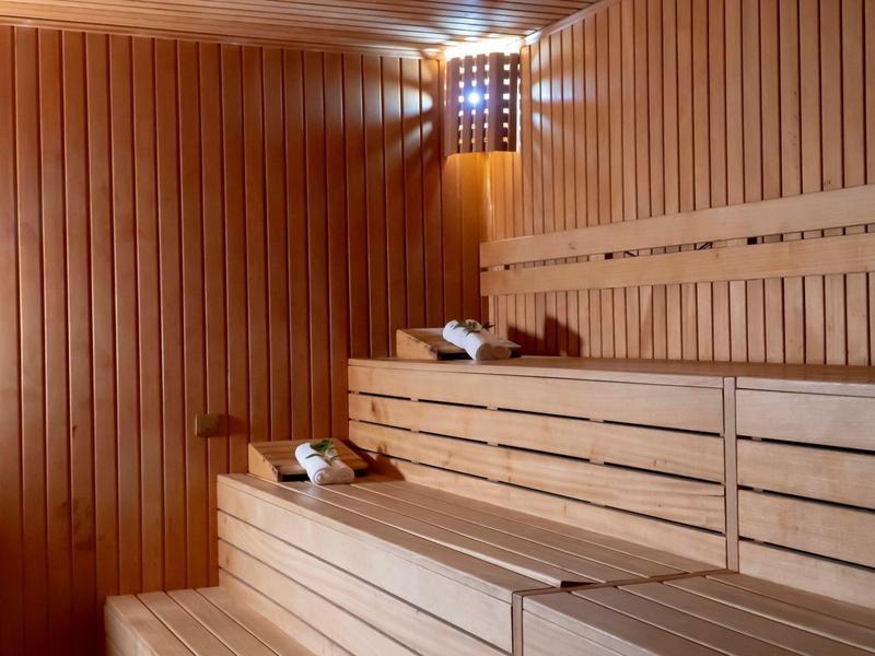 Drewniana sauna z wielopoziomowymi ławkami i dekoracyjnym oświetleniem ściennym.