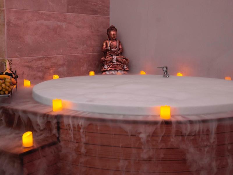 Okrągłe jacuzzi z świecami i osobą wypoczywającą w tle.