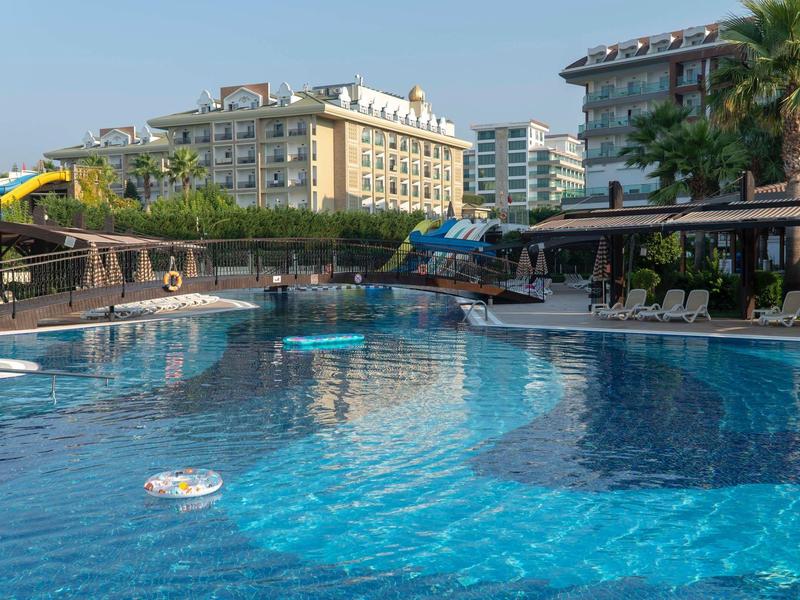 Duży basen hotelowy z zjeżdżalnią wodną i parasolami w miejskim otoczeniu.