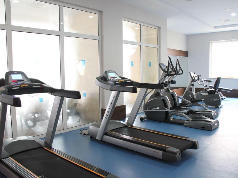 Nowoczesna siłownia z bieżniami i sprzętem fitness przy dużych oknach.