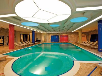 Binnenzwembad met bubbelbad, ligstoelen en kleurrijke pilaren onder zacht licht.