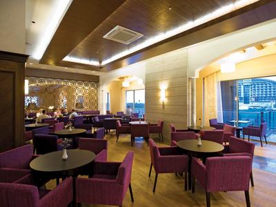 Moderne hotel/lounge met paarse stoelen, ronde tafels en grote ramen met uitzicht op water.