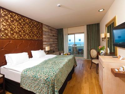 Habitación de hotel con dos camas, suelo de madera, TV, escritorio y balcón con vista al mar.