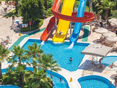 Kleurrijke glijbanen leiden naar een groot zwembad omringd door parasols en palmbomen.