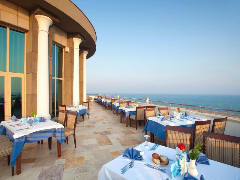 Buiten eetgedeelte met gedekte tafels en uitzicht op de zee onder een heldere blauwe lucht.