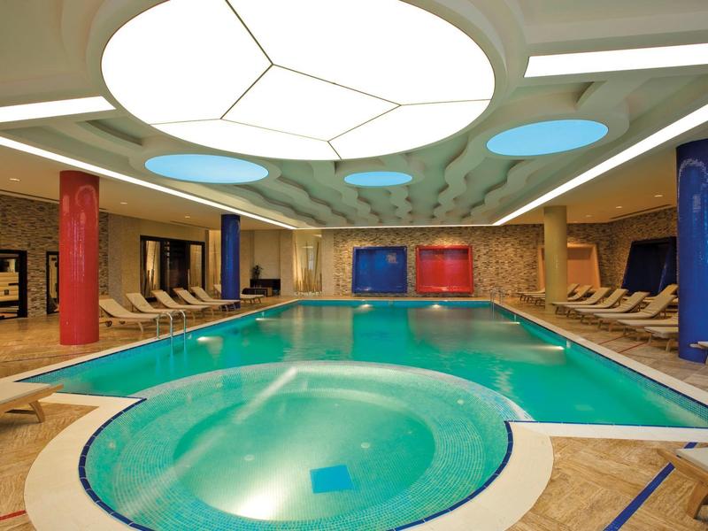 Binnenzwembad met bubbelbad, ligstoelen en kleurrijke zuilen in een hotel spa gebied.