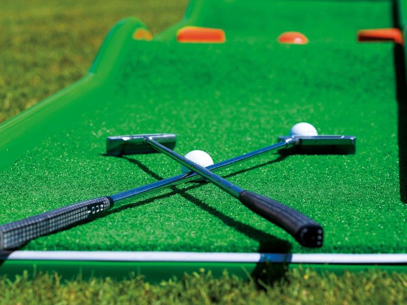 Twee golfclubs gekruist op een groene minigolfbaan met twee witte golfballen.