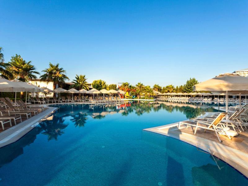 Helderblauw zwembad omringd door ligstoelen en parasols onder een zonnige lucht.