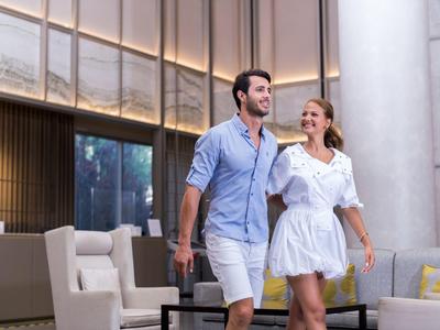 Una coppia cammina ridendo in una hall d'hotel moderna con comode poltrone.