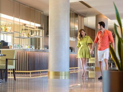 Coppia con valigie cammina in un moderno atrio dell'hotel con piante e sedie.