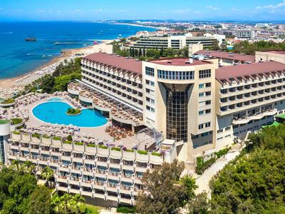 Grande hotel con più piscine vicino a una spiaggia con mare blu e cielo limpido.