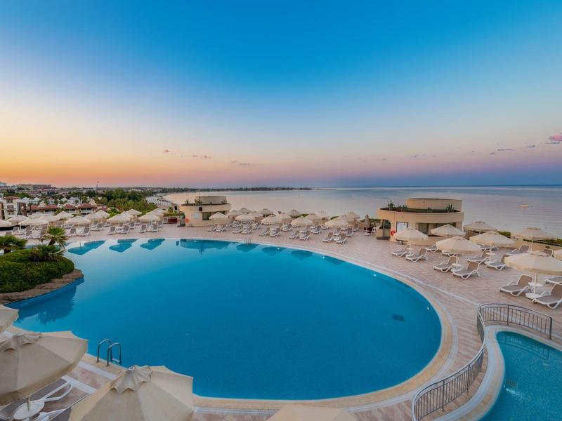 Grande piscina con lettini e ombrelloni vicino al mare al tramonto.